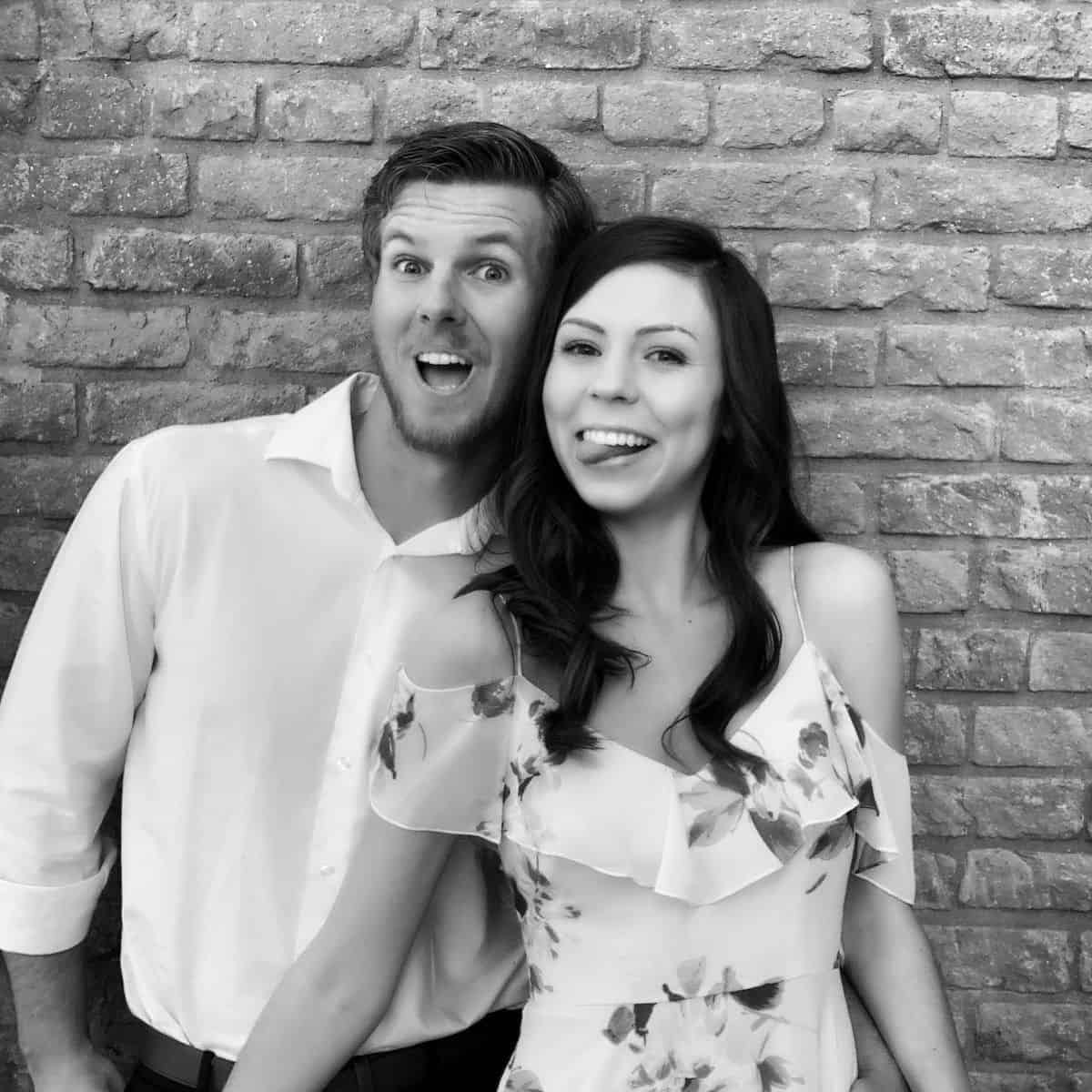 A couple posing for a photo booth photo in front of a brick wall in black and white picture