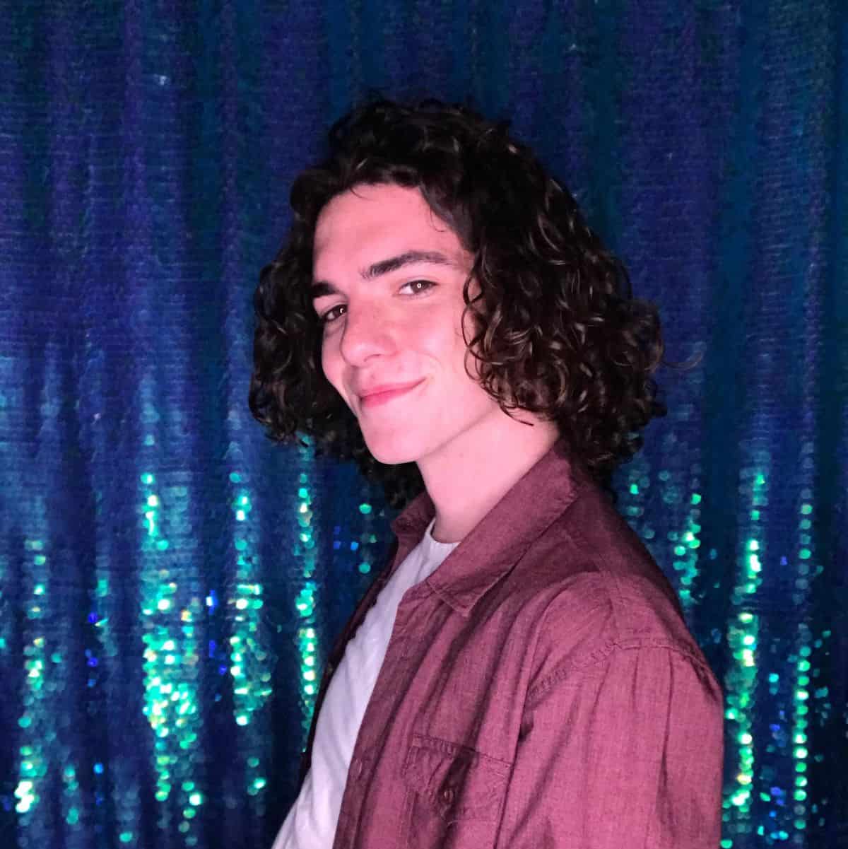 A young man smiling for his photo booth photo against a sequin backdrop